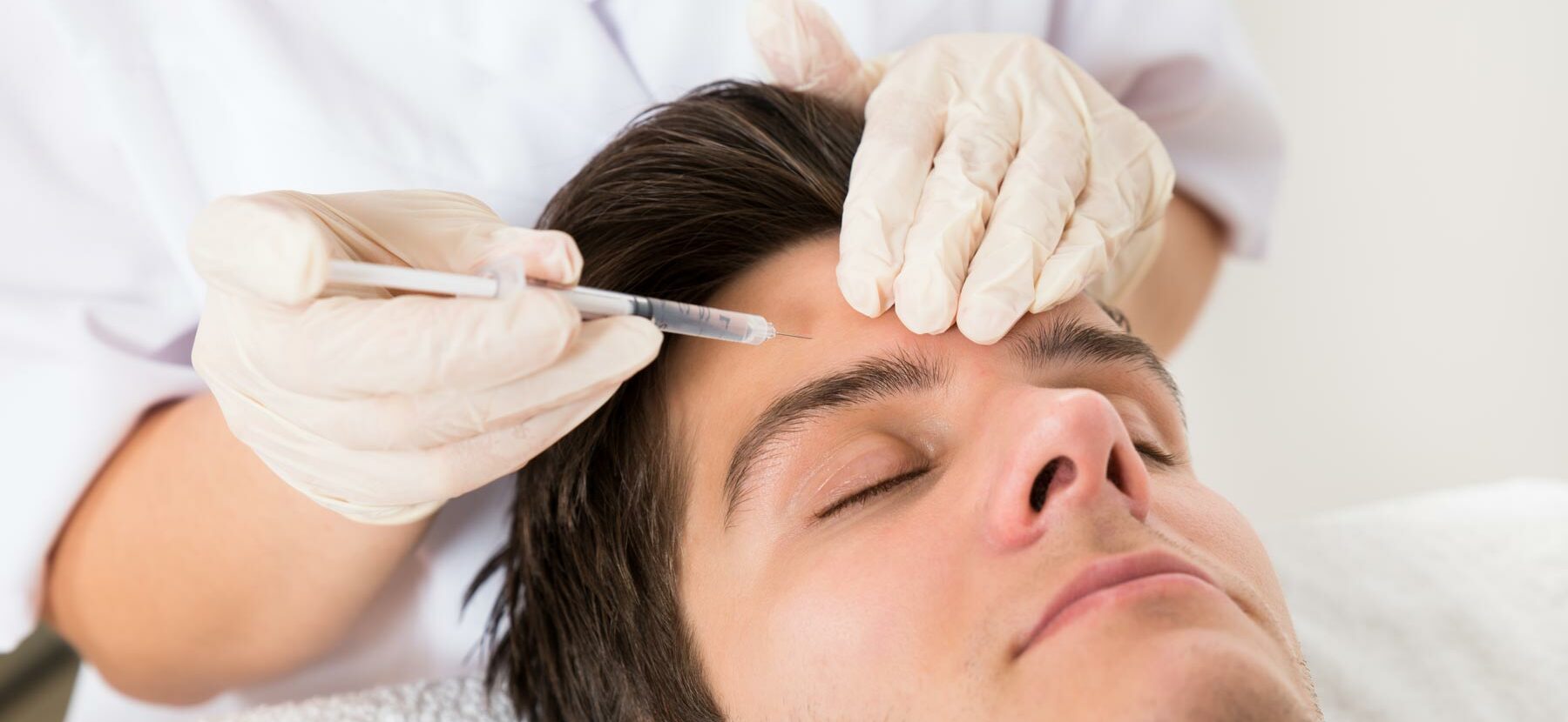Facharzt injiziert einem Mann Botulinumtoxin als Anti-Aging-Behandlung in die Stirn.